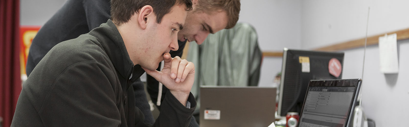 Two students are working on their computers. They are focused on their projects and looking away from the camera.